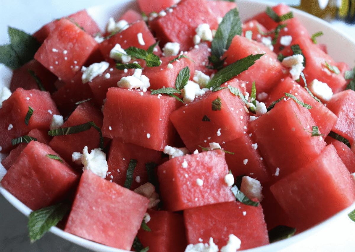 Watermelon mint salad topped with crumbled feta in a white serving bowl. 