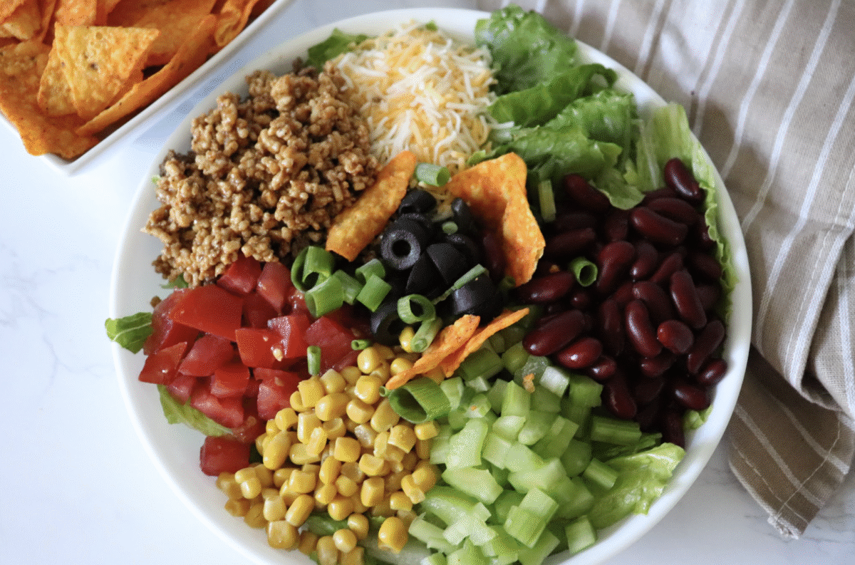 Southwest summer salad with kidney beans, corn, ground beef and corn chips in a serving bowl with a striped linen.