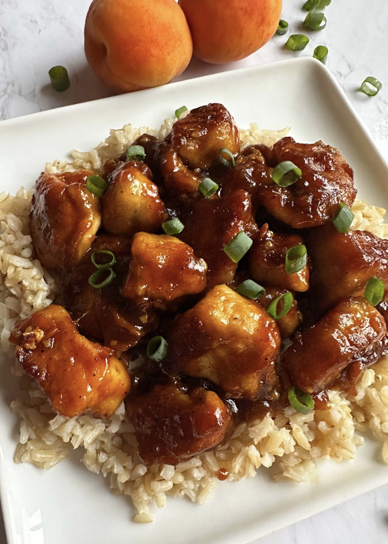 sticky apricot chicken topped with green onions and served over rice on a white plate.