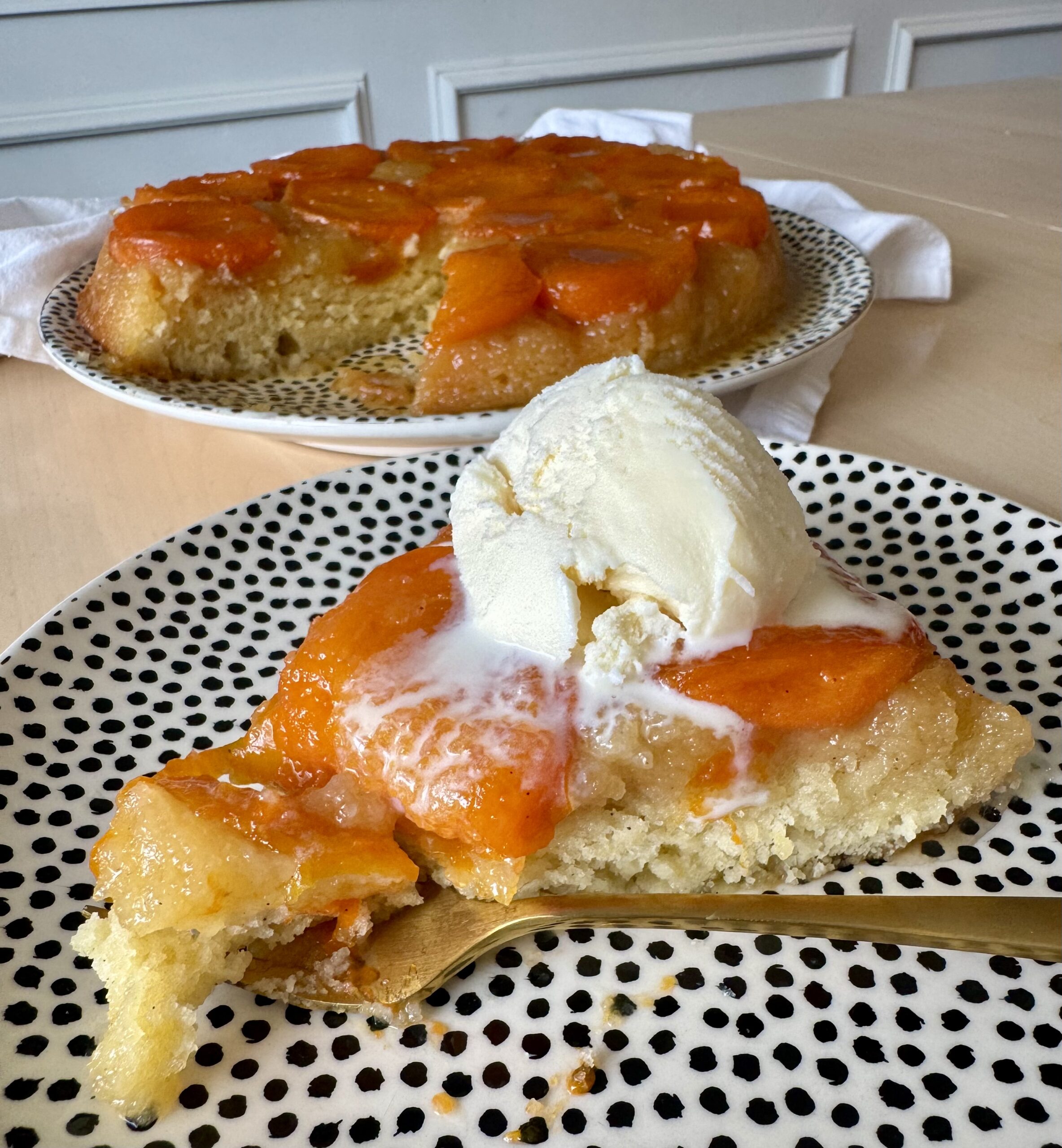 A slice of apricot tart on a serving plate topped with vanilla ice cream.