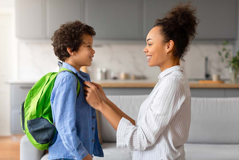 Smiling mother putting a denim jacket on her son who is ready to go back to school after a successful morning routine