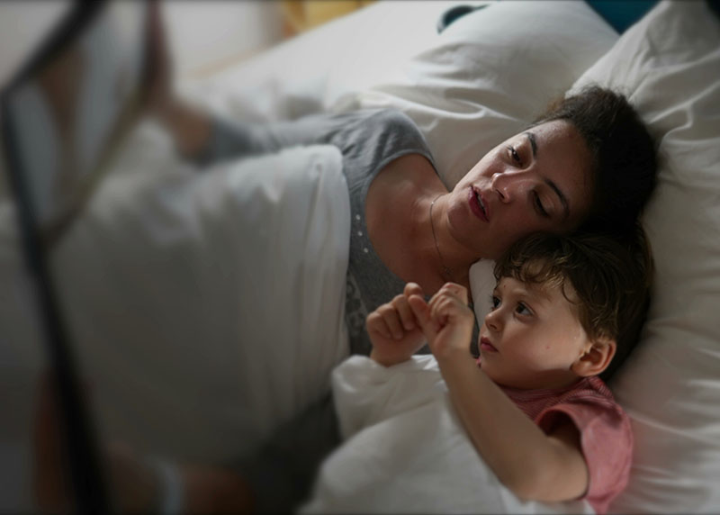 A mother reading a bedtime story to her son while lying in bed, developing strong family habits