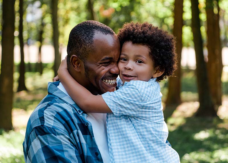 African American father and son hugging and smiling, wearing blue shirts, in a park, developing strong family habits