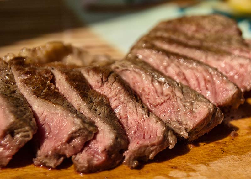 Cooked flank steak on a wood cutting board, sliced across the grain, for Steak fajita bowls with cilantro lime rice
