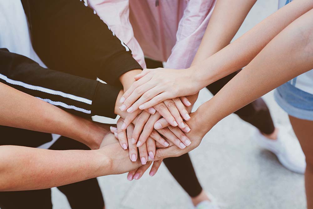 Group of women with in a circle with hands all in the center in a show of support to help manage challenges as parents of sending kids back-to-school