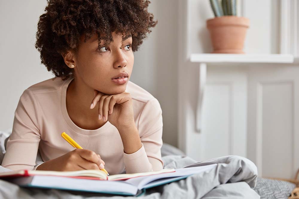 Woman laying on her bed and writing in her journal as she deals with the anxiety of sending her kids back-to-school