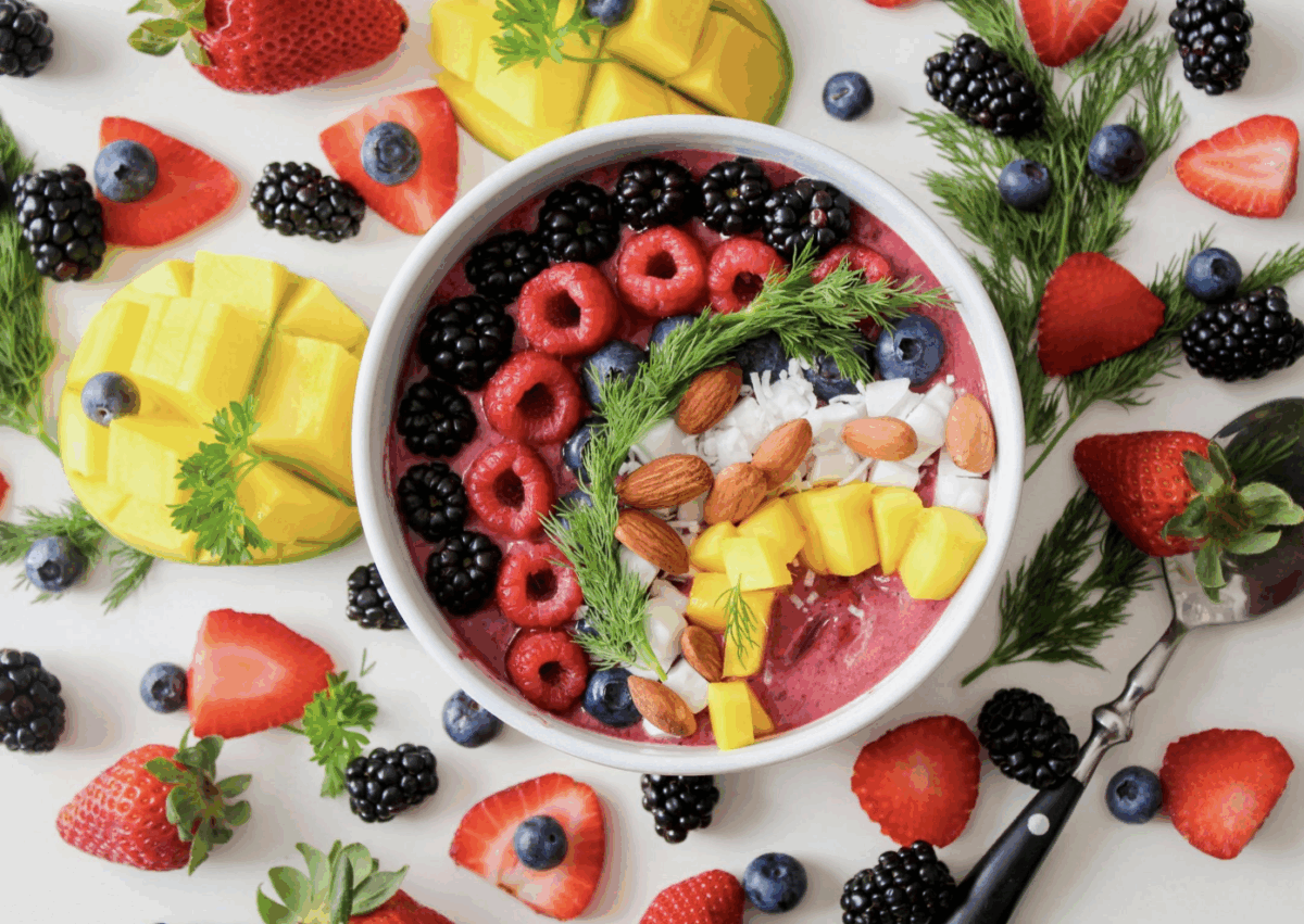 a colorful acai bowl topped with different fresh fruit, almonds, and fresh herbs