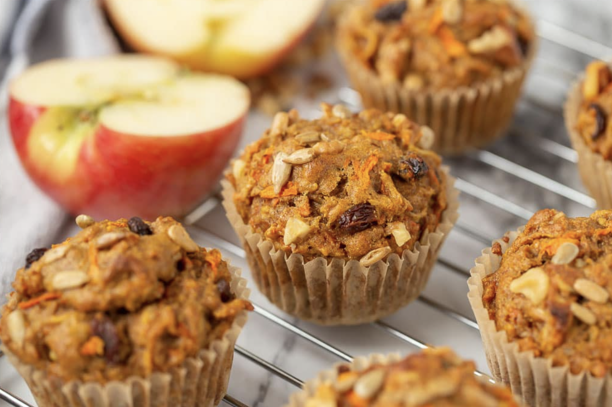 healthy morning glory muffins on a wire rack with fresh apples in the background