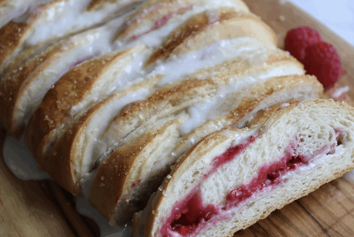 raspberry cream cheese braided bread sliced on a wooden cutting board with fresh raspberries