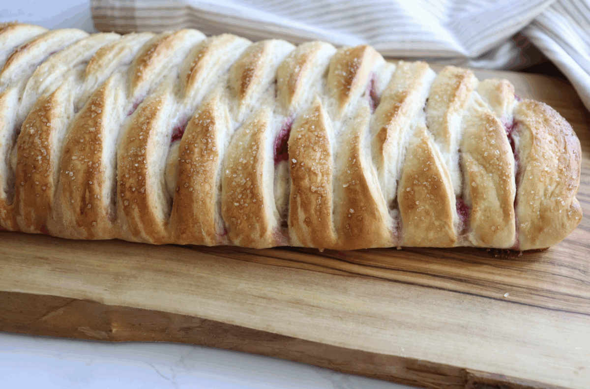 raspberry cream cheese braided bread on a wooden cutting board with a striped linen in the background
