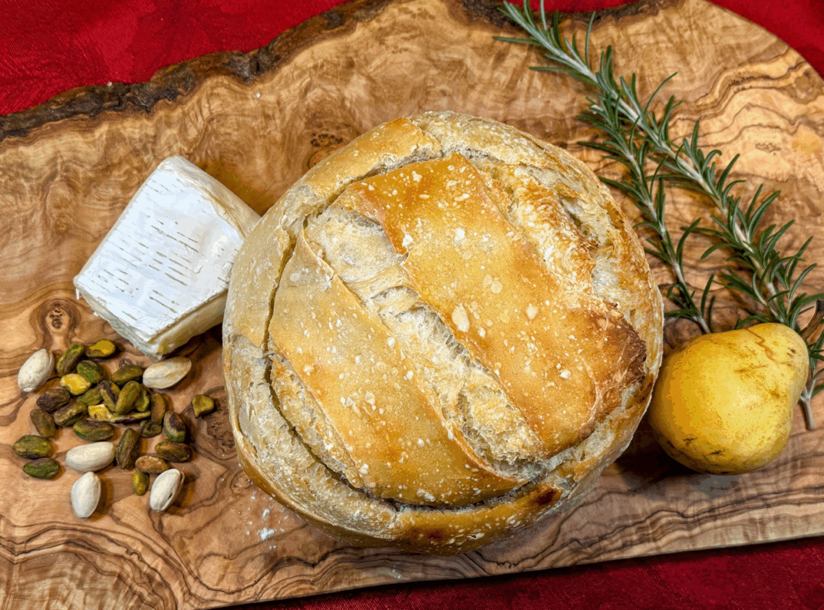 pistachio pear and brie stuffed sourdough bread with fresh pears, rosemary and pistachios on a cutting board