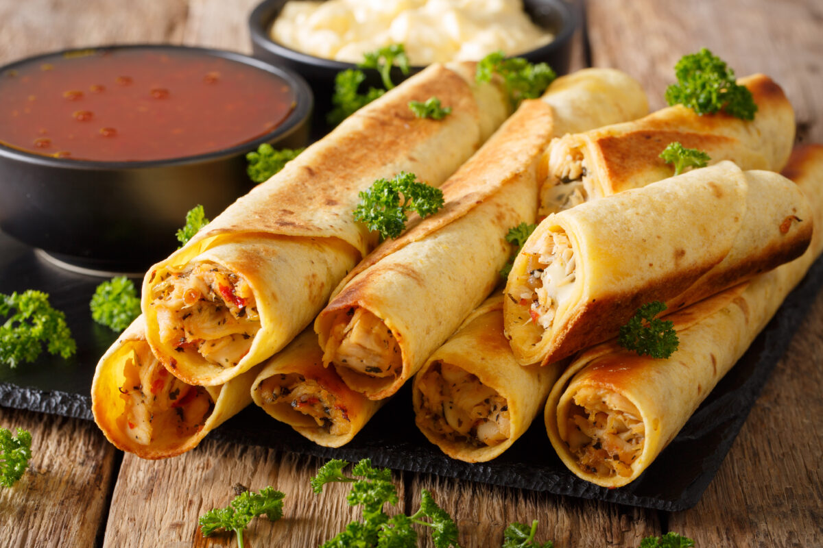creamy baked chicken taquitos on a serving plate with salsa and cheese