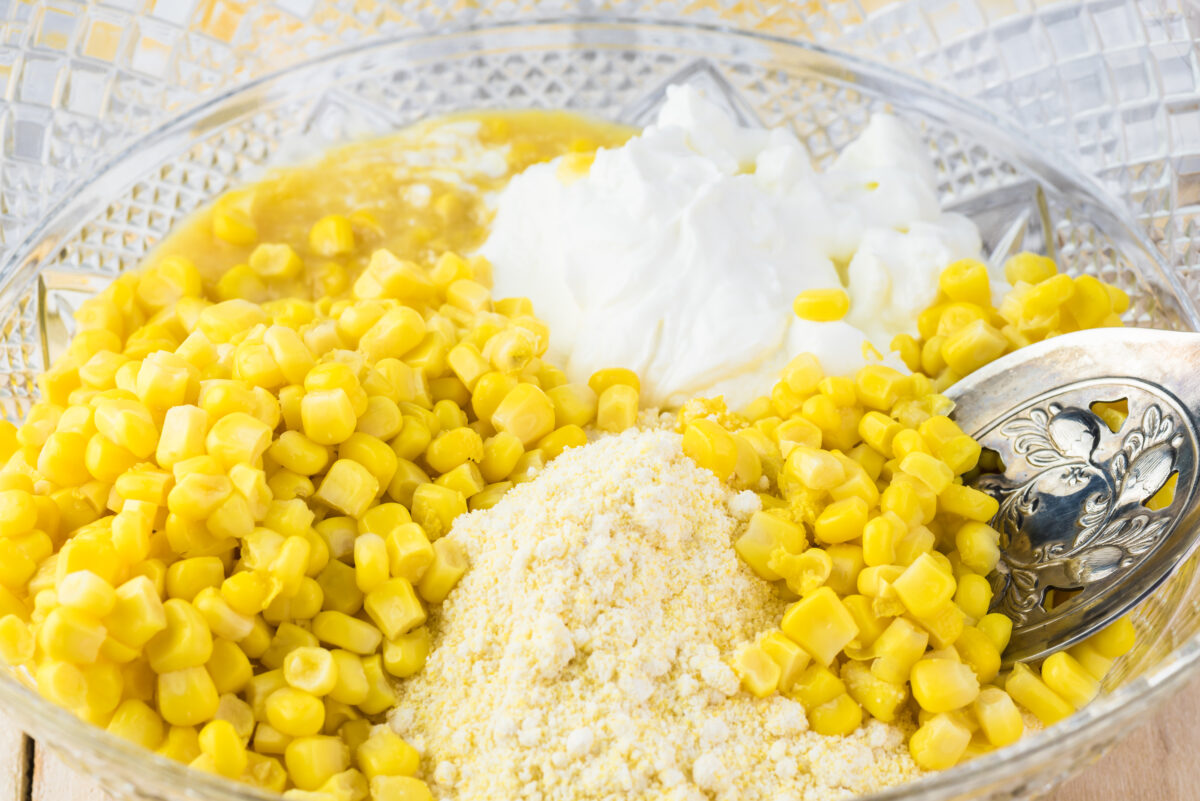 Close up of bowl with mixed of kernel corn, sour cream, butter, creamy corn, mix corn flour - ingredients for creamy cheese corn casserole.