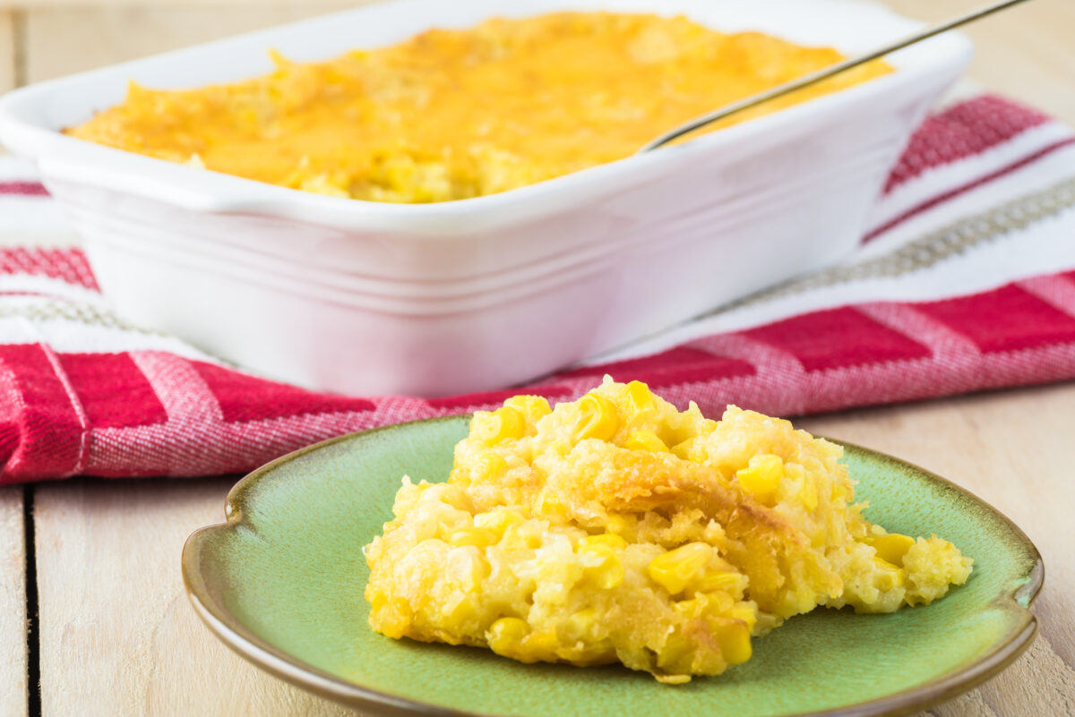 Close up of casserole dish and green plate with fresh baked homemade creamy cheese corn casserole.