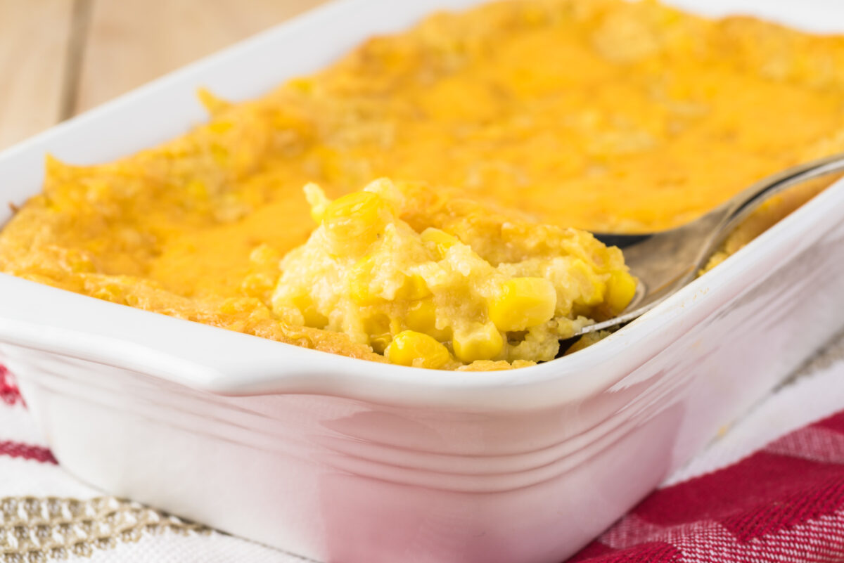creamy corn casserole in a white ceramic baking dish with a serving spoon