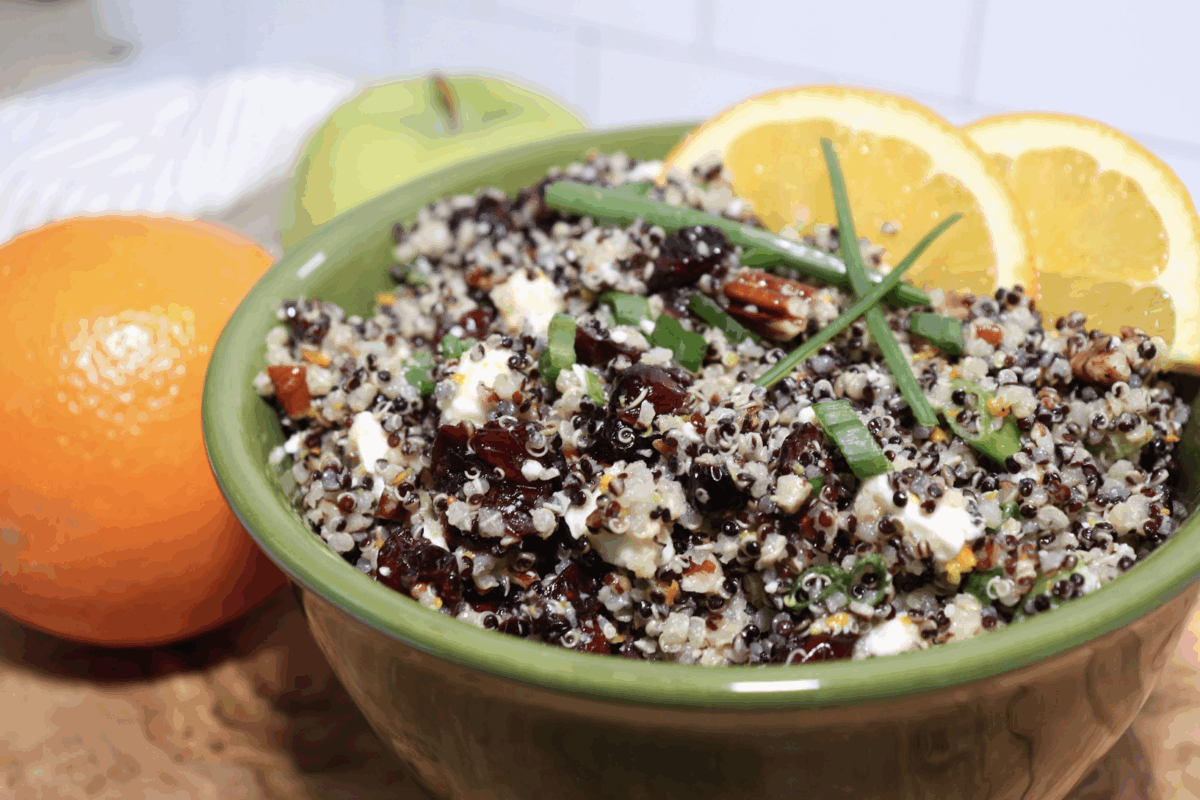 cranberry quinoa salad topped with green onions and orange slices in a green serving bowl
