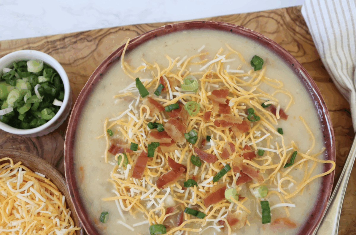crockpot potato soup in a serving bowl with shredded cheese, bacon, and green onions