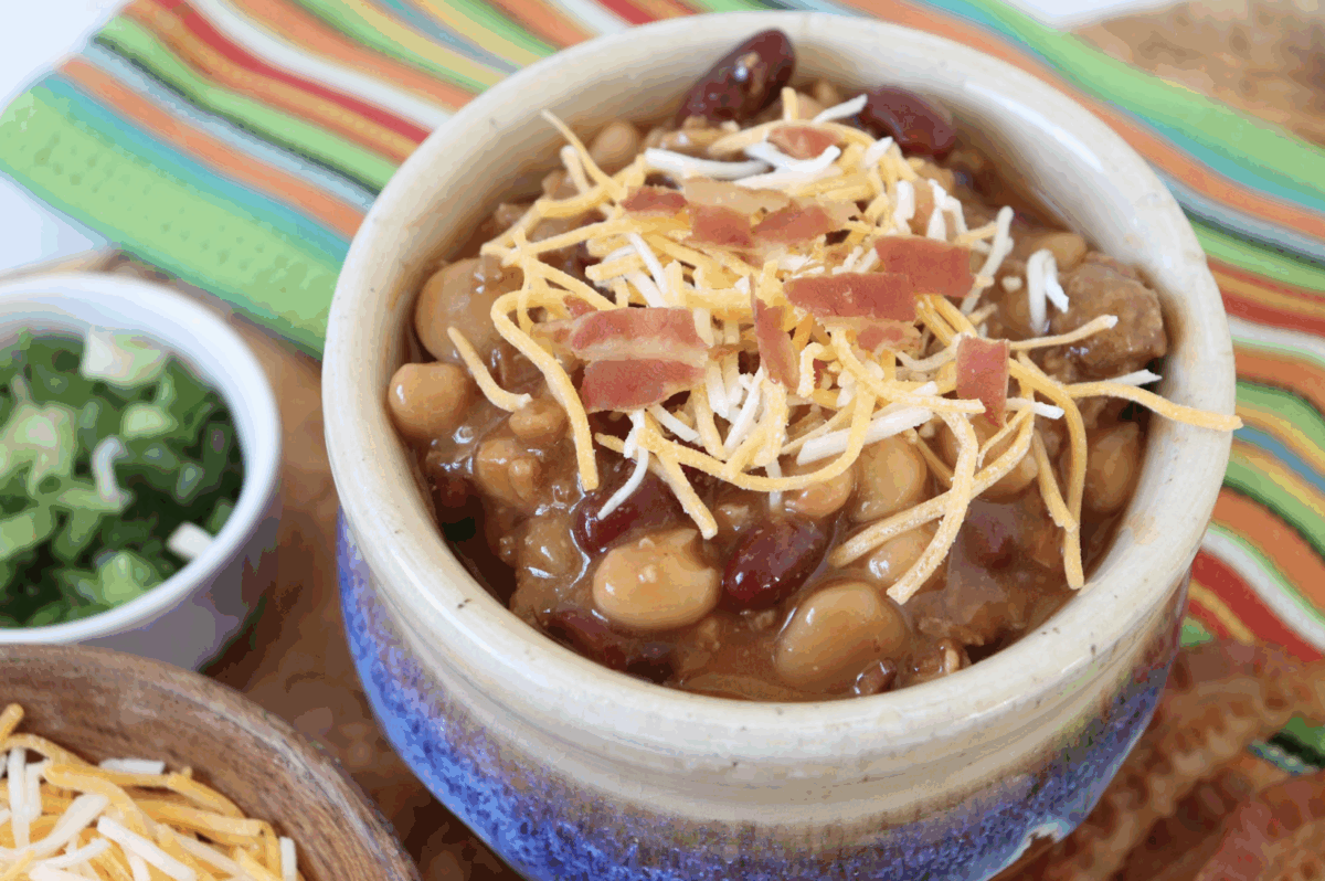 a bowl of chili topped with cheese and bacon with a side of green onions