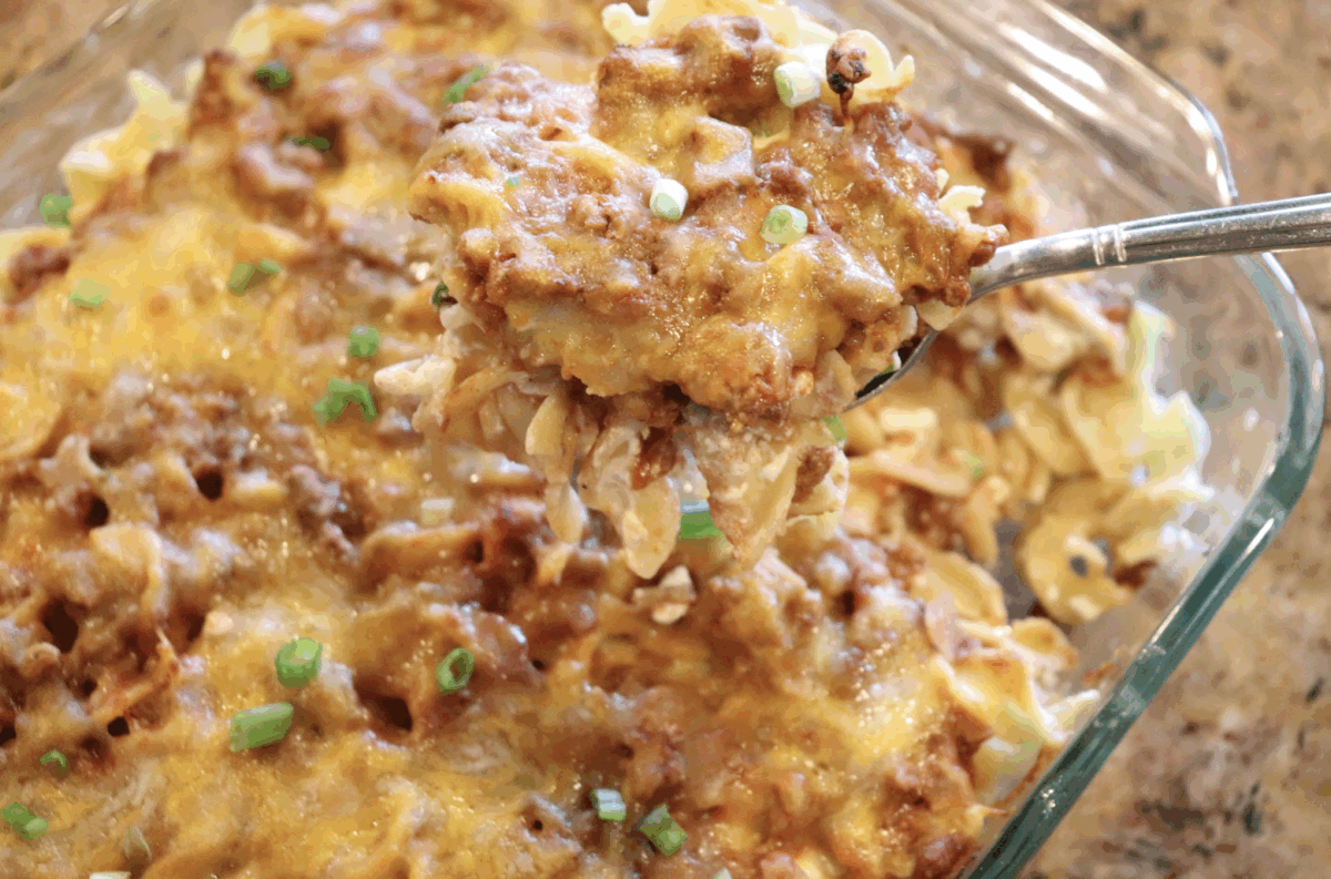 noodle casserole in a glass dish being scooped out with a serving spoon