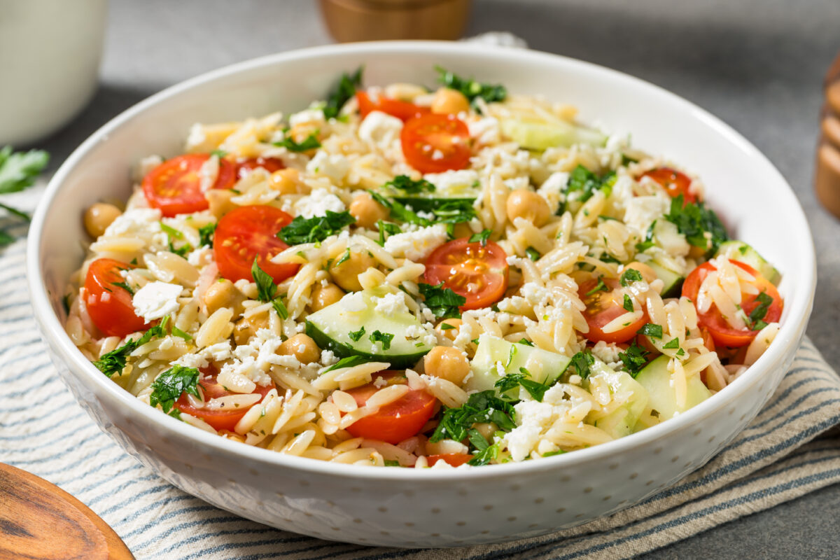 greek orzo pasta salad in a white serving bowl with a striped linen