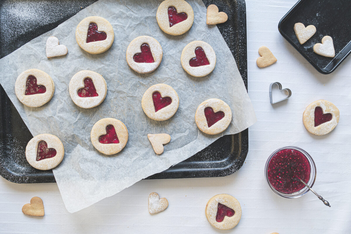 a cookie sheet with linzer cookies and a bowl of raspberry jam
