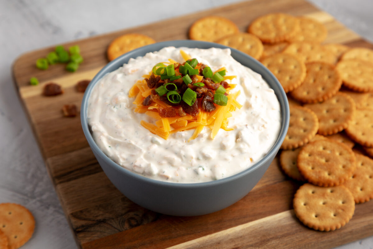 high protein crack dip with cheddar cheese, bacon and green onions in a serving bowl with ritz crackers