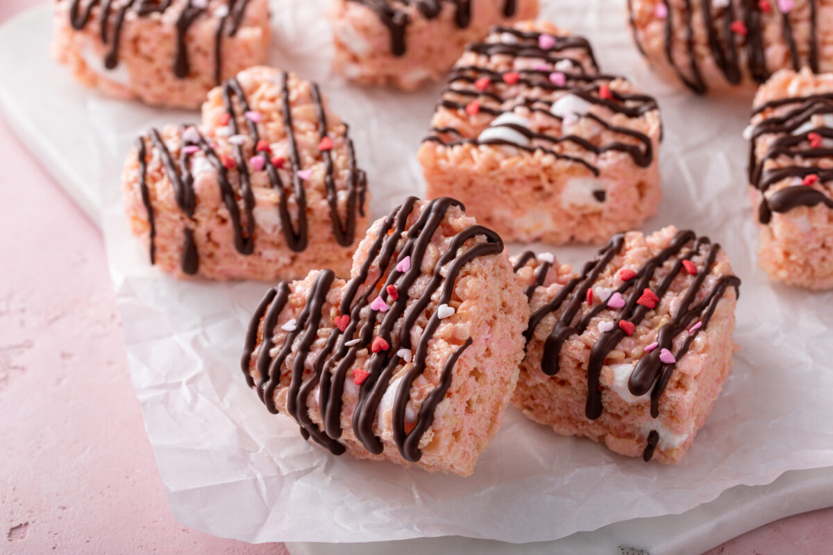 Pink heart shaped rice krispie treats drizzled with dark chocolate on a cooling rack, homemade sweet treat on a marble board