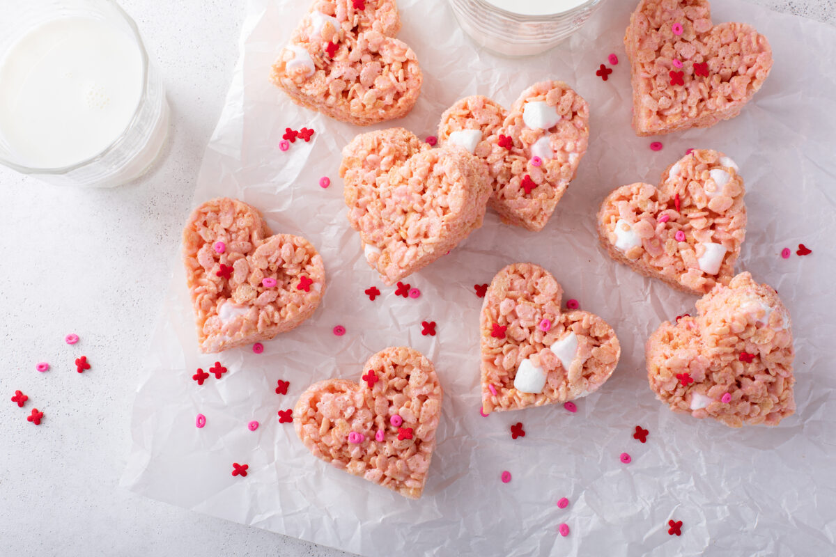 strawberry rice krispie treats cut into hearts and topped with sprinkles on a sheet of parchment paper
