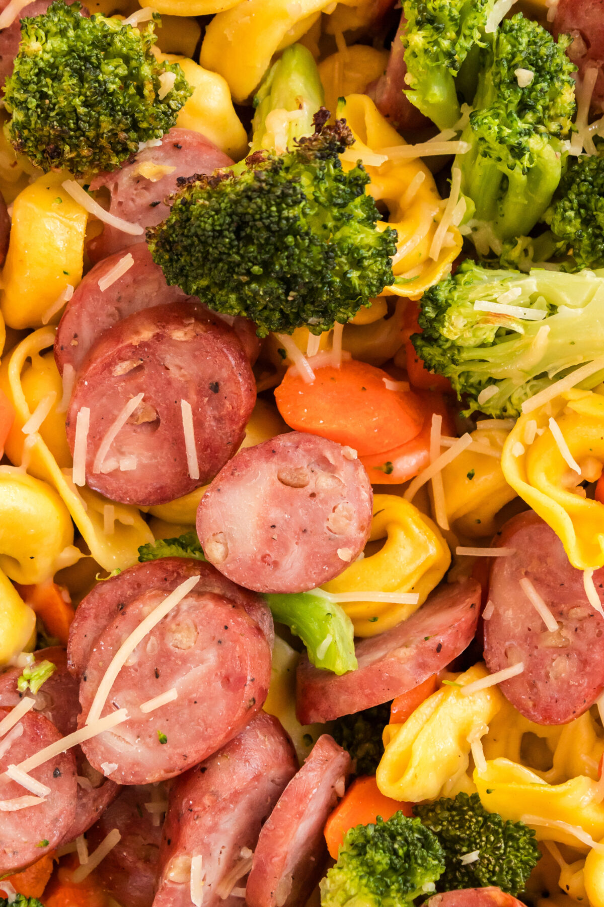 a close up image of tortellini bake with kielbasa, carrots and broccoli