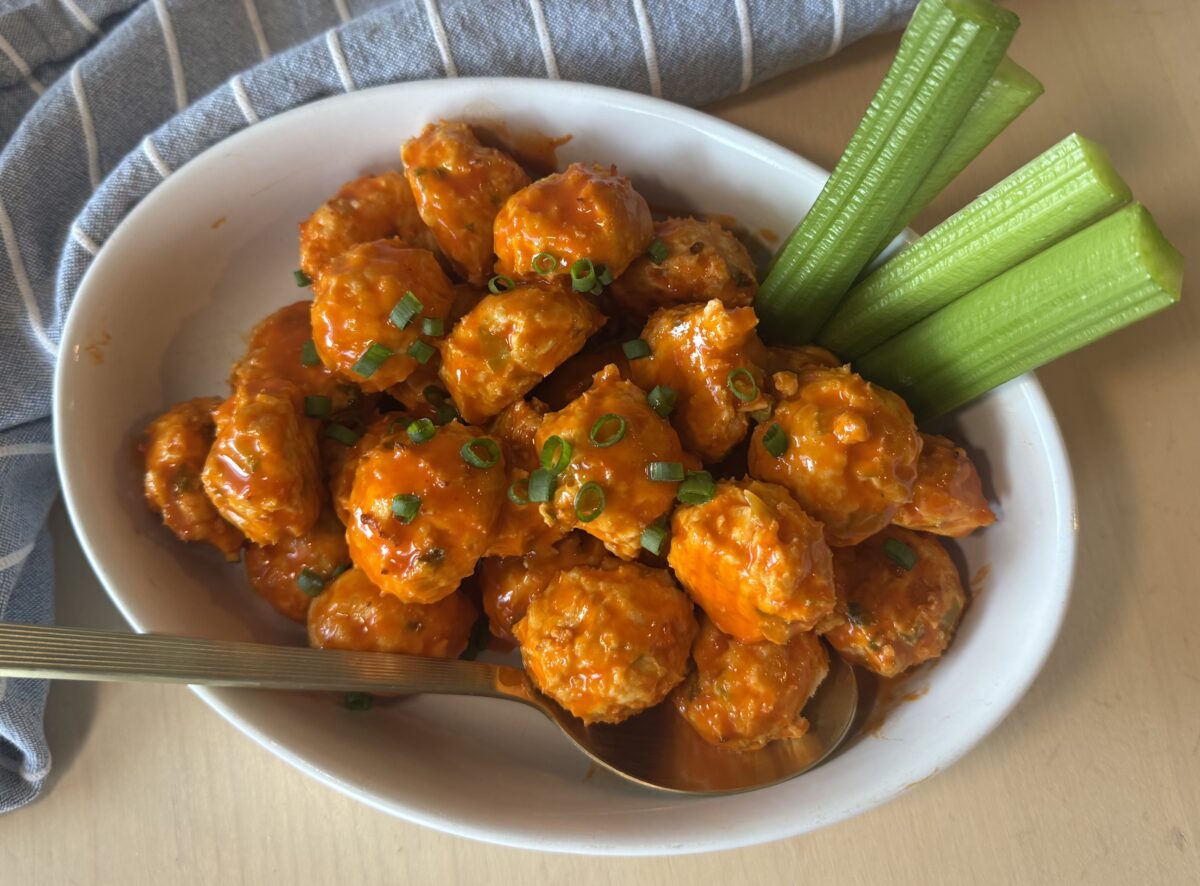 buffalo chicken meatballs with celery sticks in a serving dish topped with sliced green onions