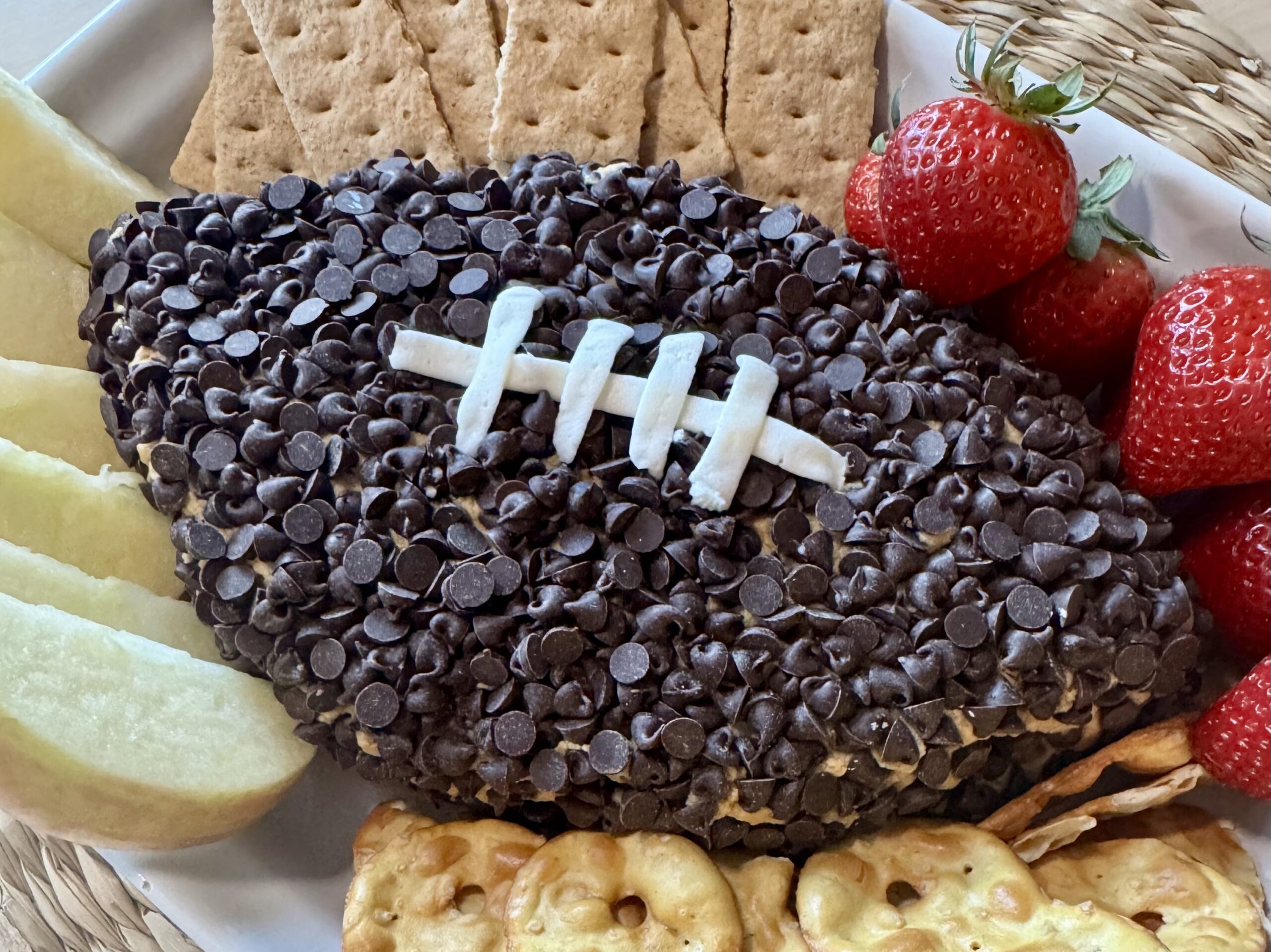 peanut butter dip with chocolate chips shaped like a football and served with pretzels and fresh fruit