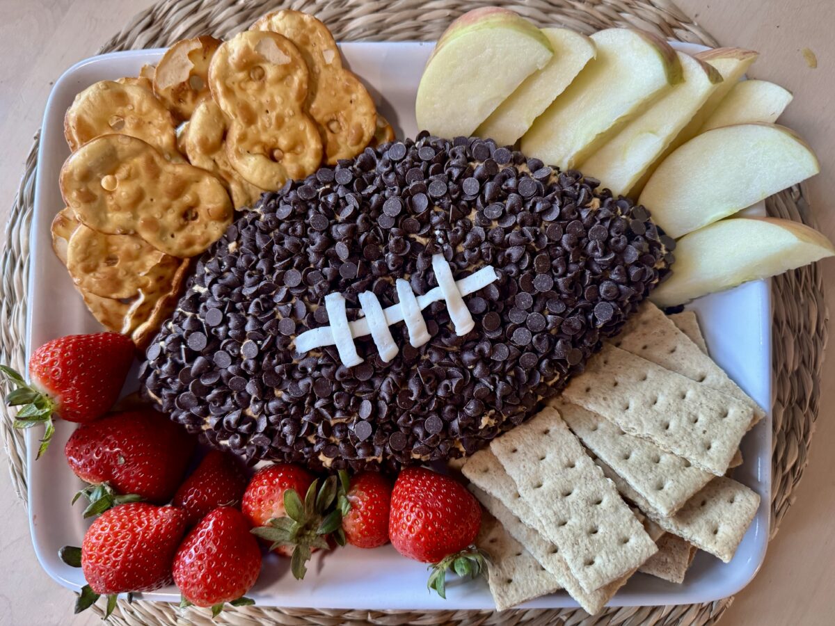 peanut butter dip with chocolate chips shaped like a football and served with pretzels and fresh fruit