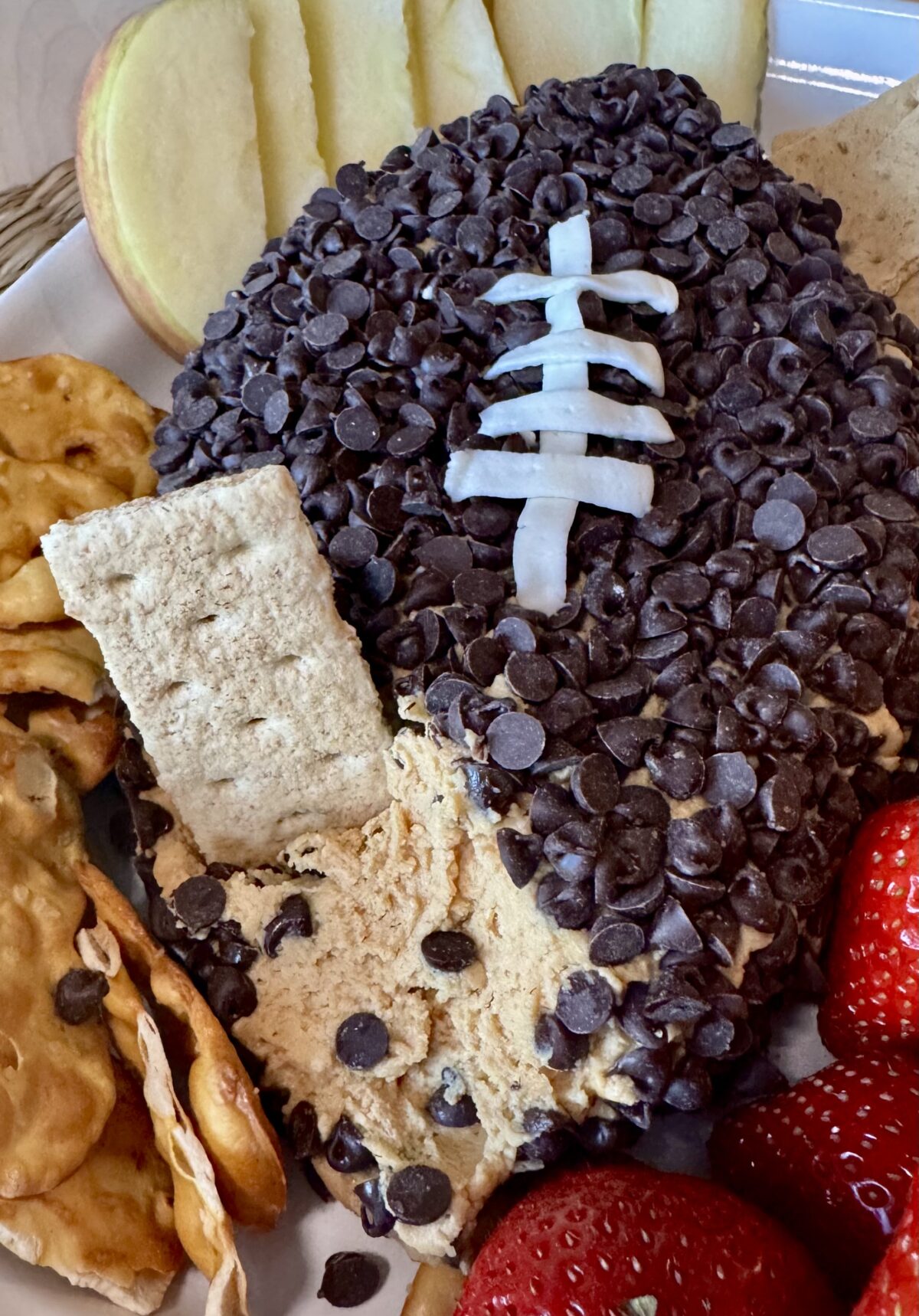 peanut butter football dip a with graham cracker dipped into it and fresh fruit on the side.