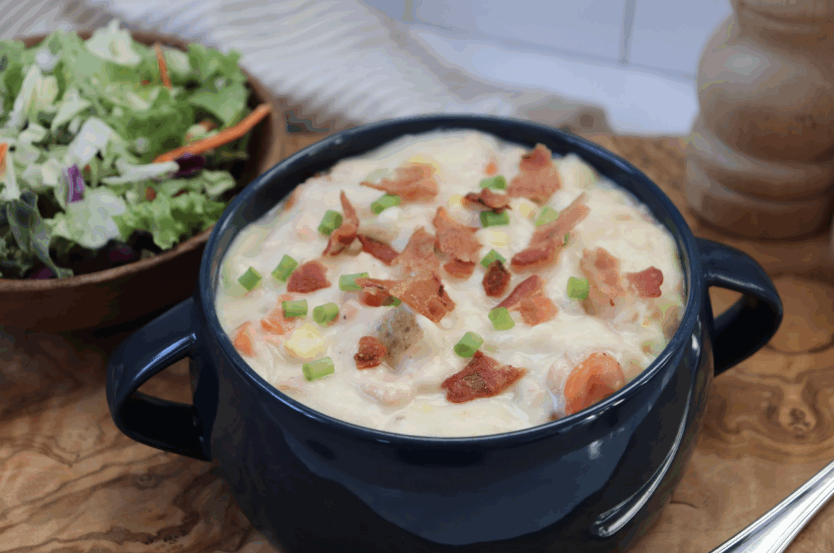 salmon chowder in a serving bowl topped with bacon and sliced green onions served with a side salad