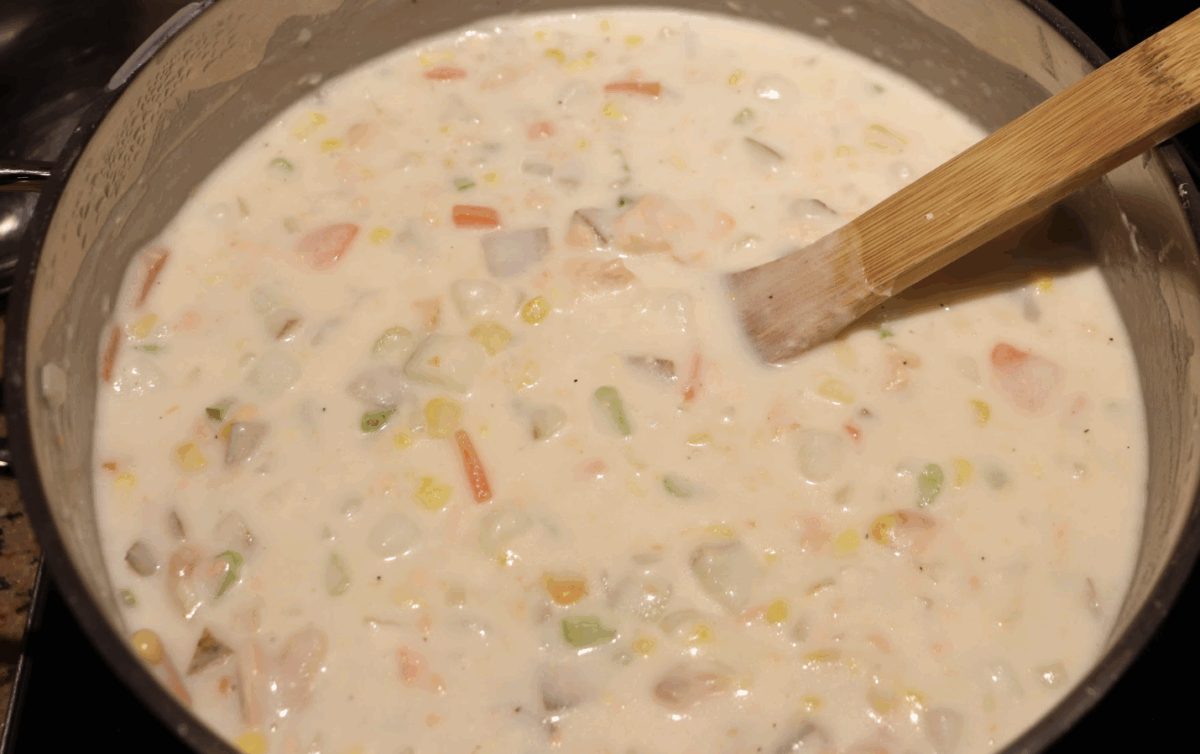creamy salmon chowder in a pot with a large wooden spoon