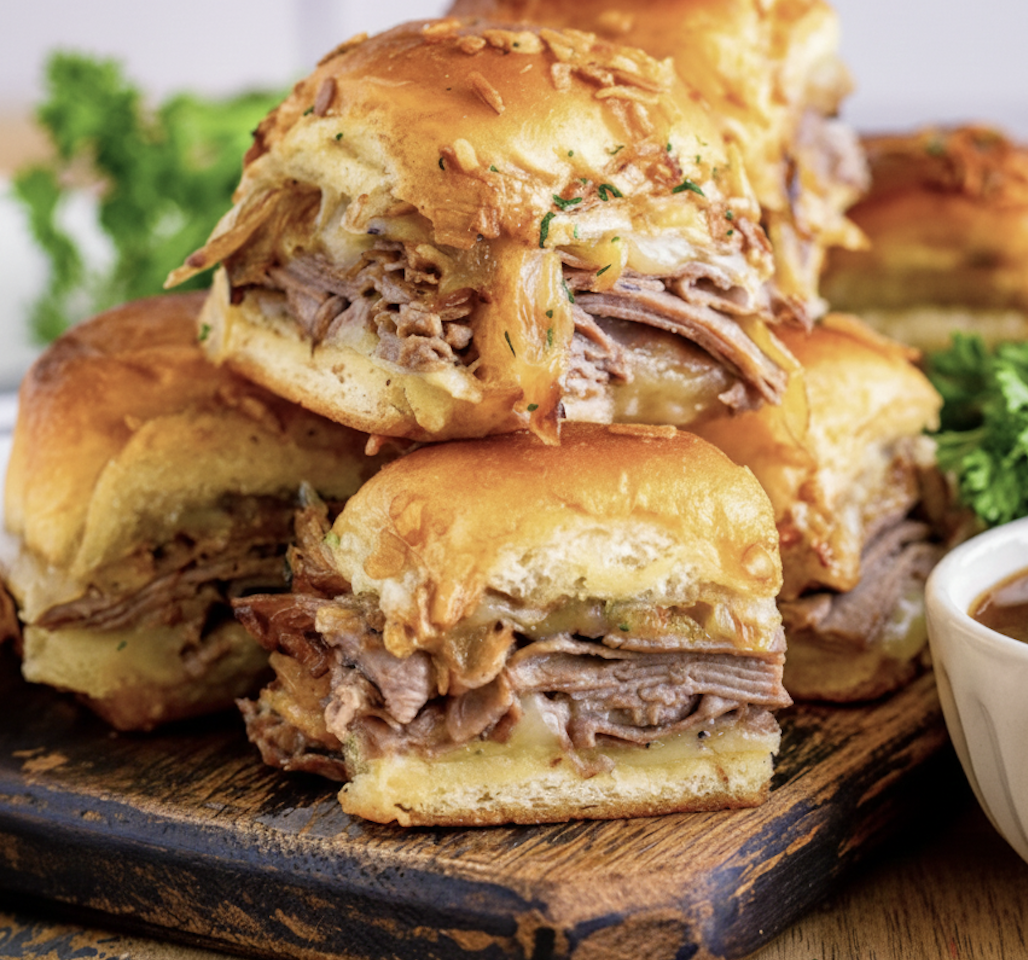 french dip sliders with melted cheese and caramelized onions on a wooden board