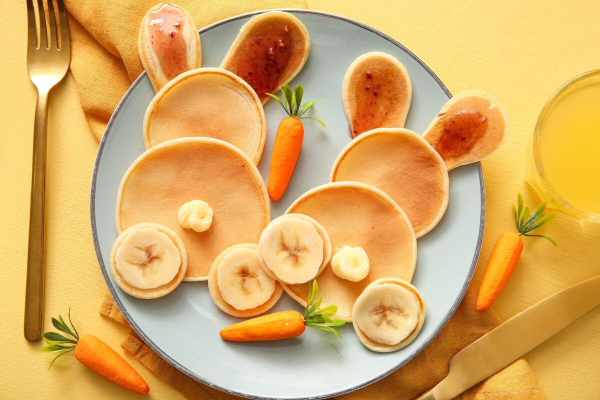 Funny Easter bunny pancakes with banana and glass of orange juice on yellow background