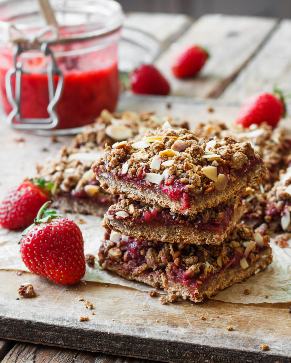 strawberry oat bars stacked on a piece of parchment with fresh strawberries