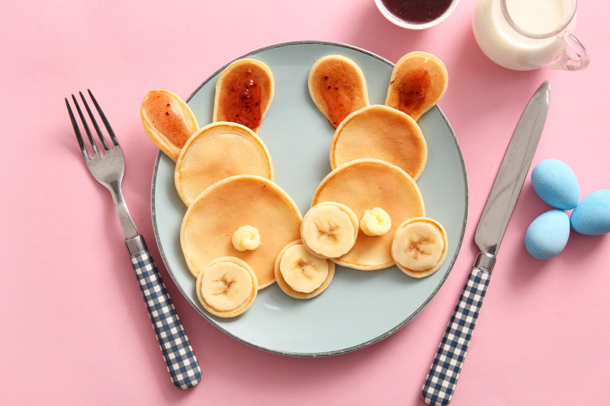 Funny Easter bunny pancakes with banana and painted eggs on pink background