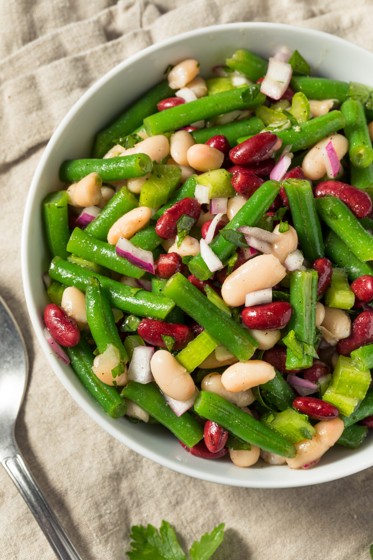 three bean salad with onion and parsley in a serving bowl with a spoon