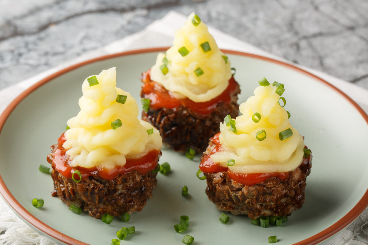 mini meatloaves topped with ketchup, a swirl of mashed potatoes and minced chives on a serving plate.