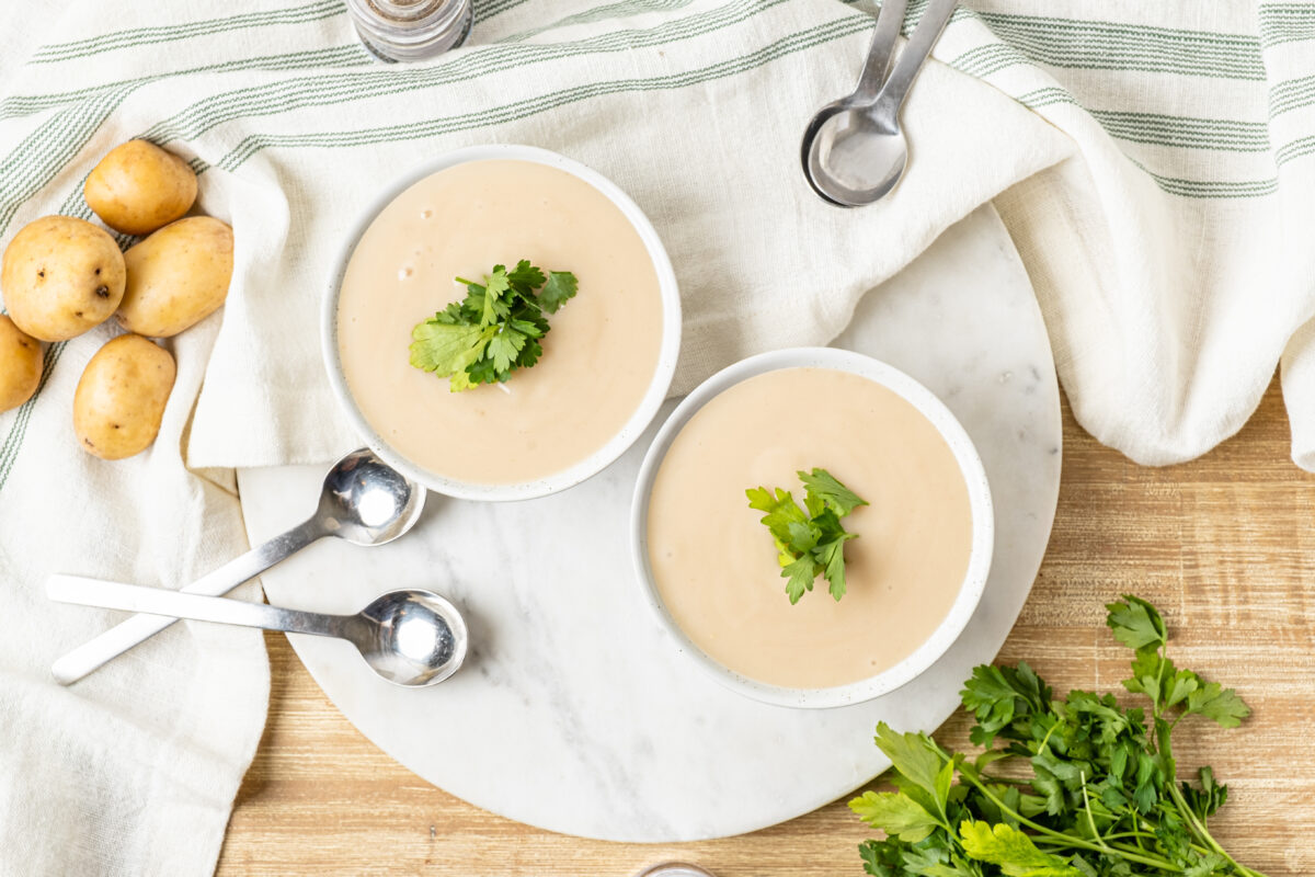 two bowls of creamy potato leek soup with fresh parsely and potatoes in the background