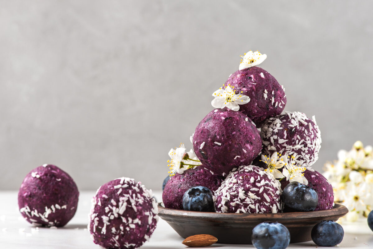 Raw vegan food dessert. Blueberry energy balls or bites made of fresh berries, nuts and dates served with flowers. Food styling