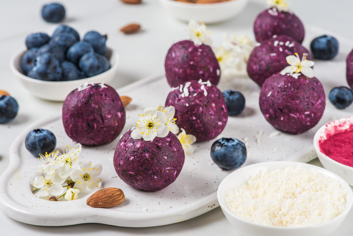 Raw vegan energy bites or balls made of blueberry, acai, nuts and dates served with flowers. Food styling. Healthy dessert