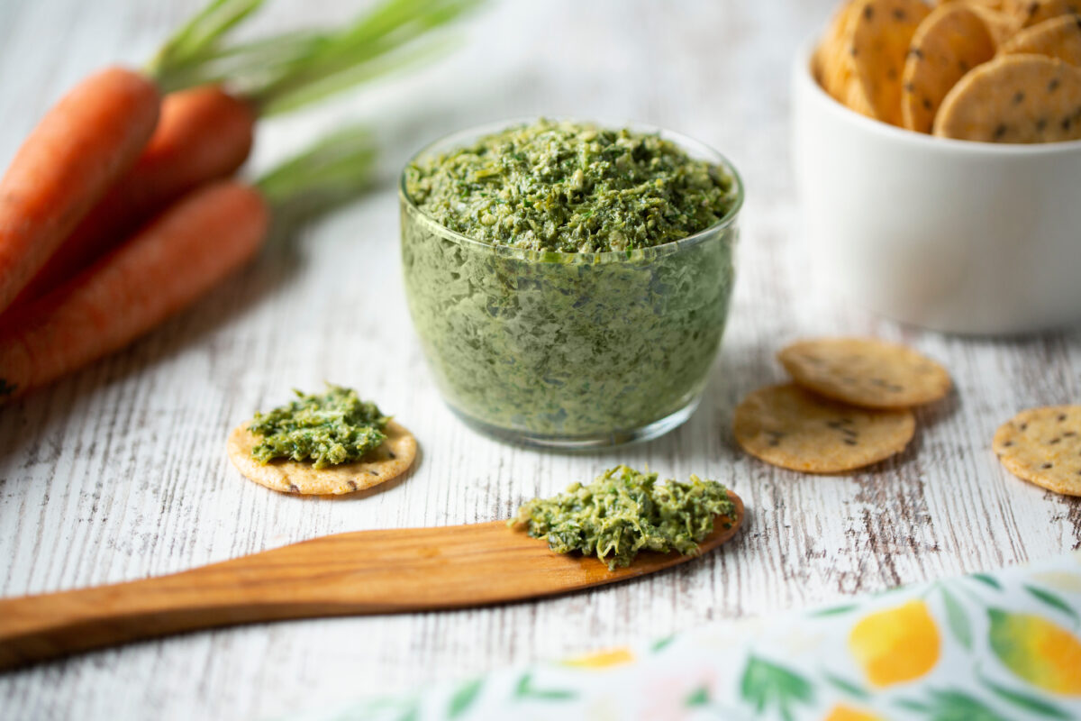 carrot top pesto in a small glass bowl with rice crackers on the side. 