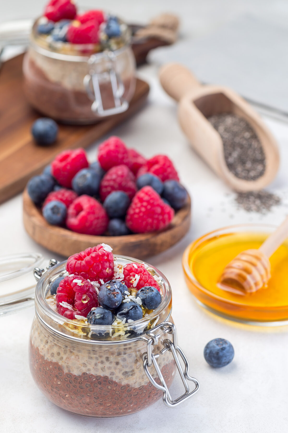 Layered chocolate and peanut butter chia seed pudding in  jar, garnished with raspberry, blueberry, honey and coconut flakes