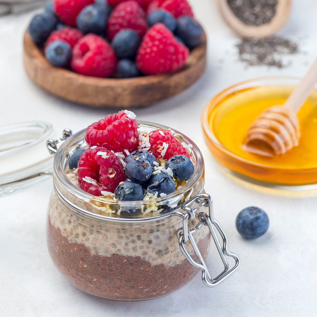 Layered chocolate and peanut butter chia seed pudding in a jar, garnished with raspberry, blueberry, honey and coconut flakes