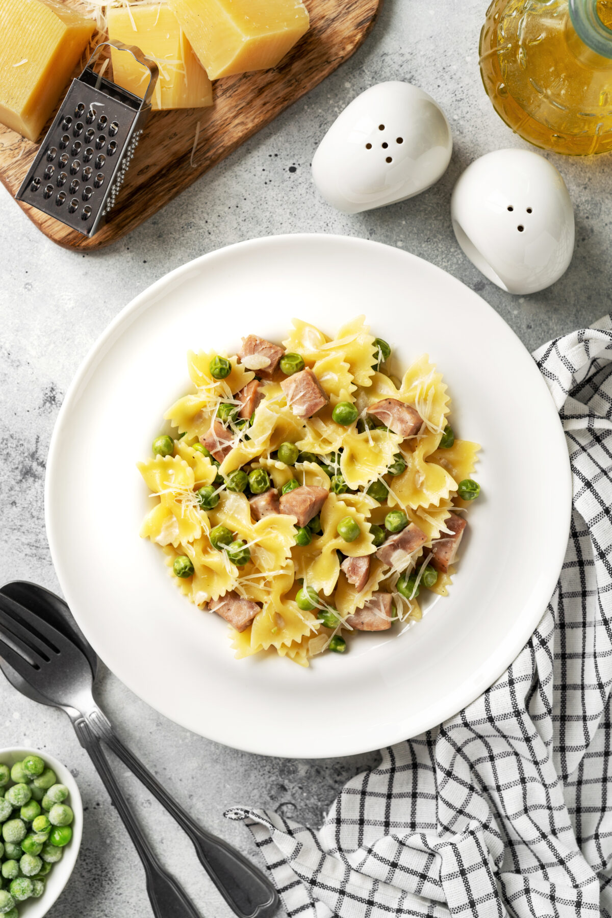 ham and bowtie pasta in a serving dish with utensils and a bowl of frozen peas