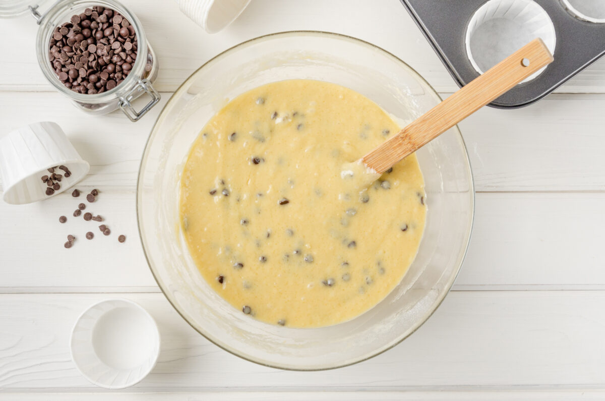 Muffin dough with chocolate chips in a bowl on a white wooden background. 