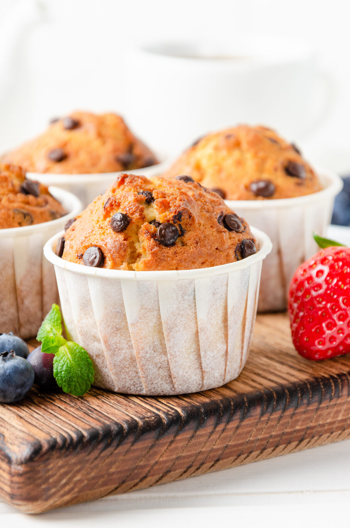 Muffins with chocolate chips on a wooden board on a white background with fresh berries.